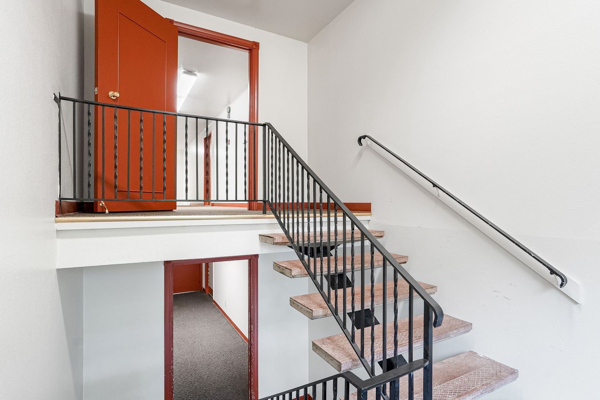 Indoor stairwell with black railing, pink carpeted steps, and orange doors on a white landing