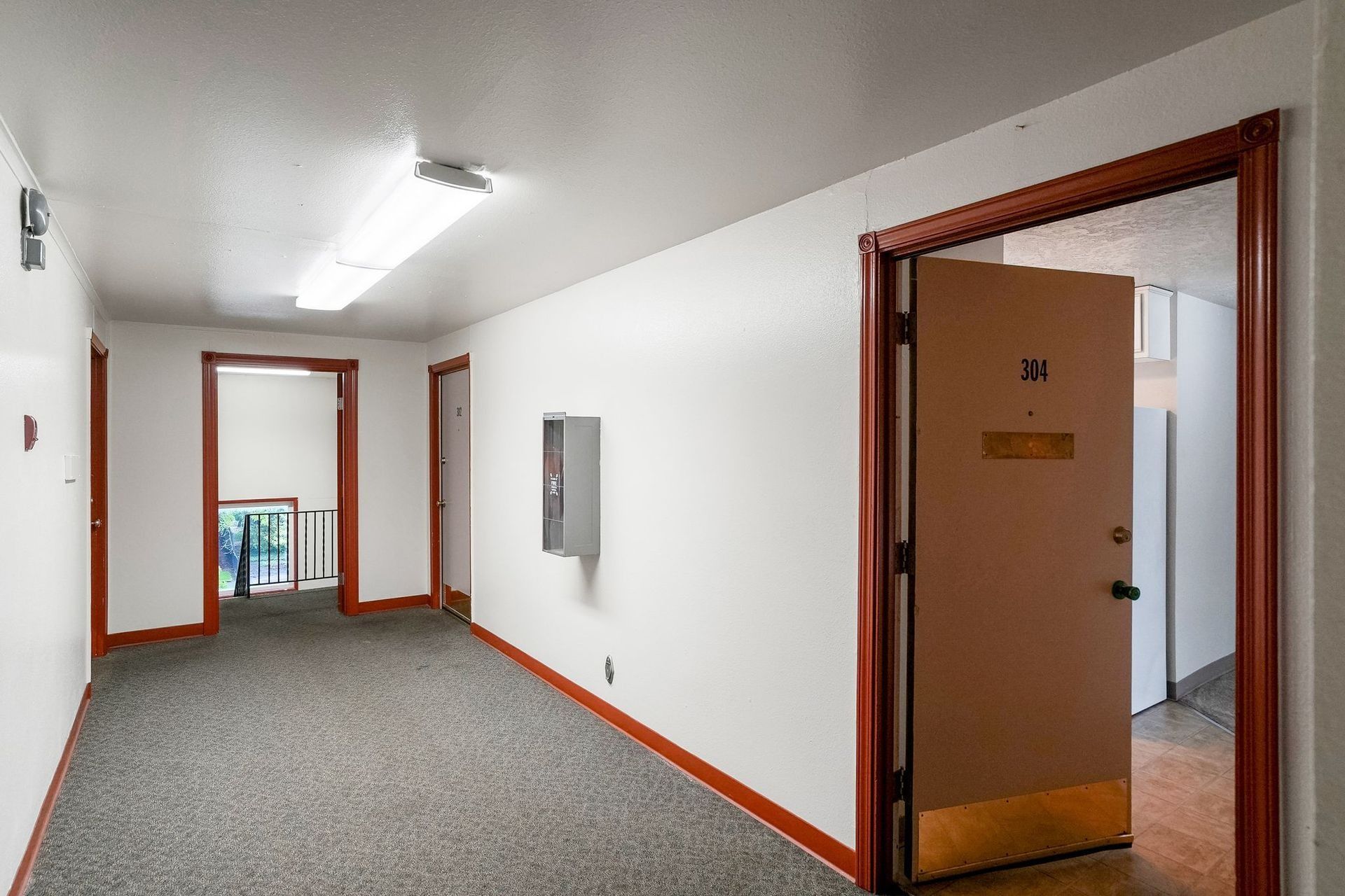 Empty apartment hallway with white walls, gray carpet, and open wooden doorways.