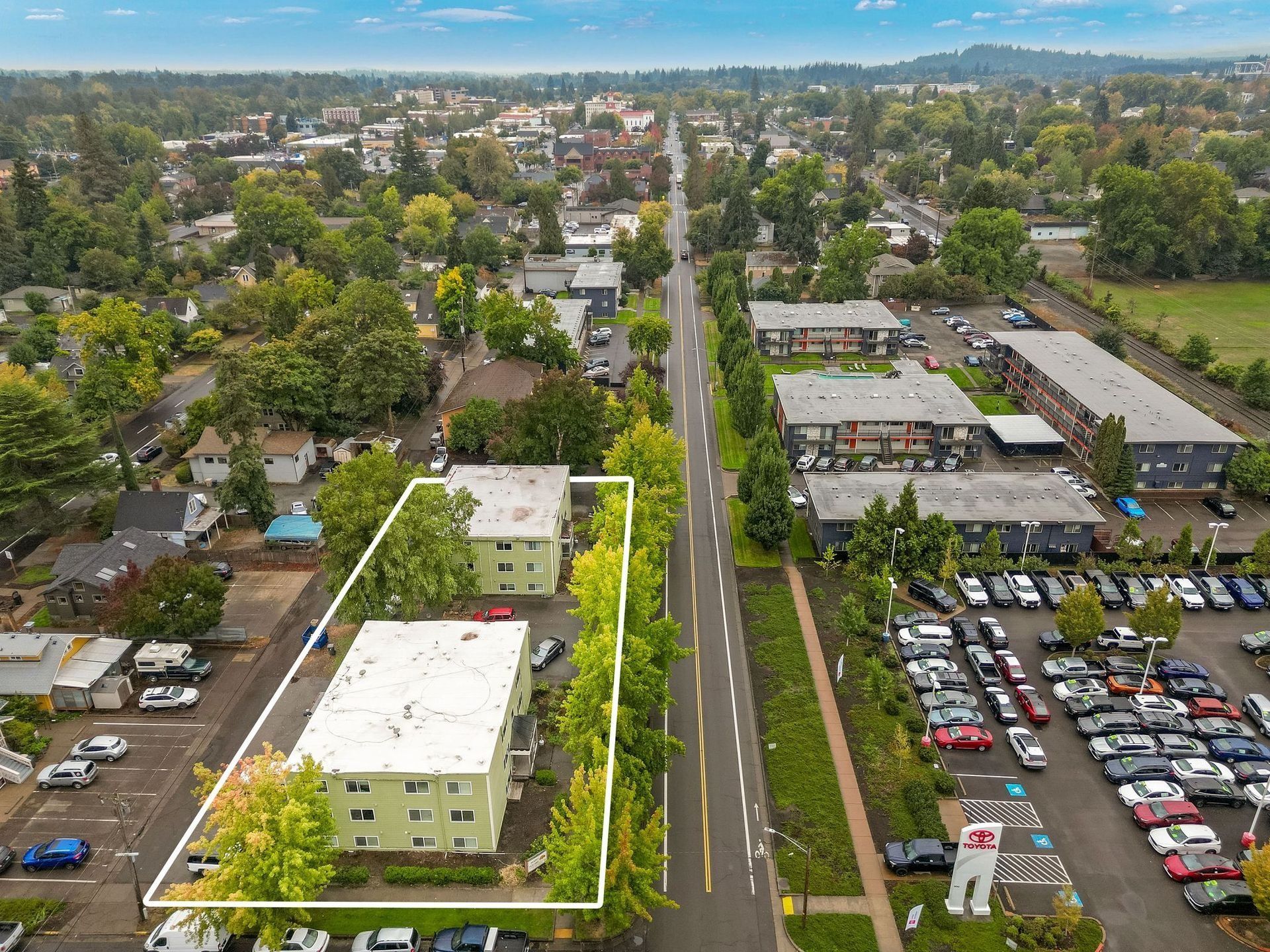Aerial view of an apartment complex beside a parking lot and tree-lined road.