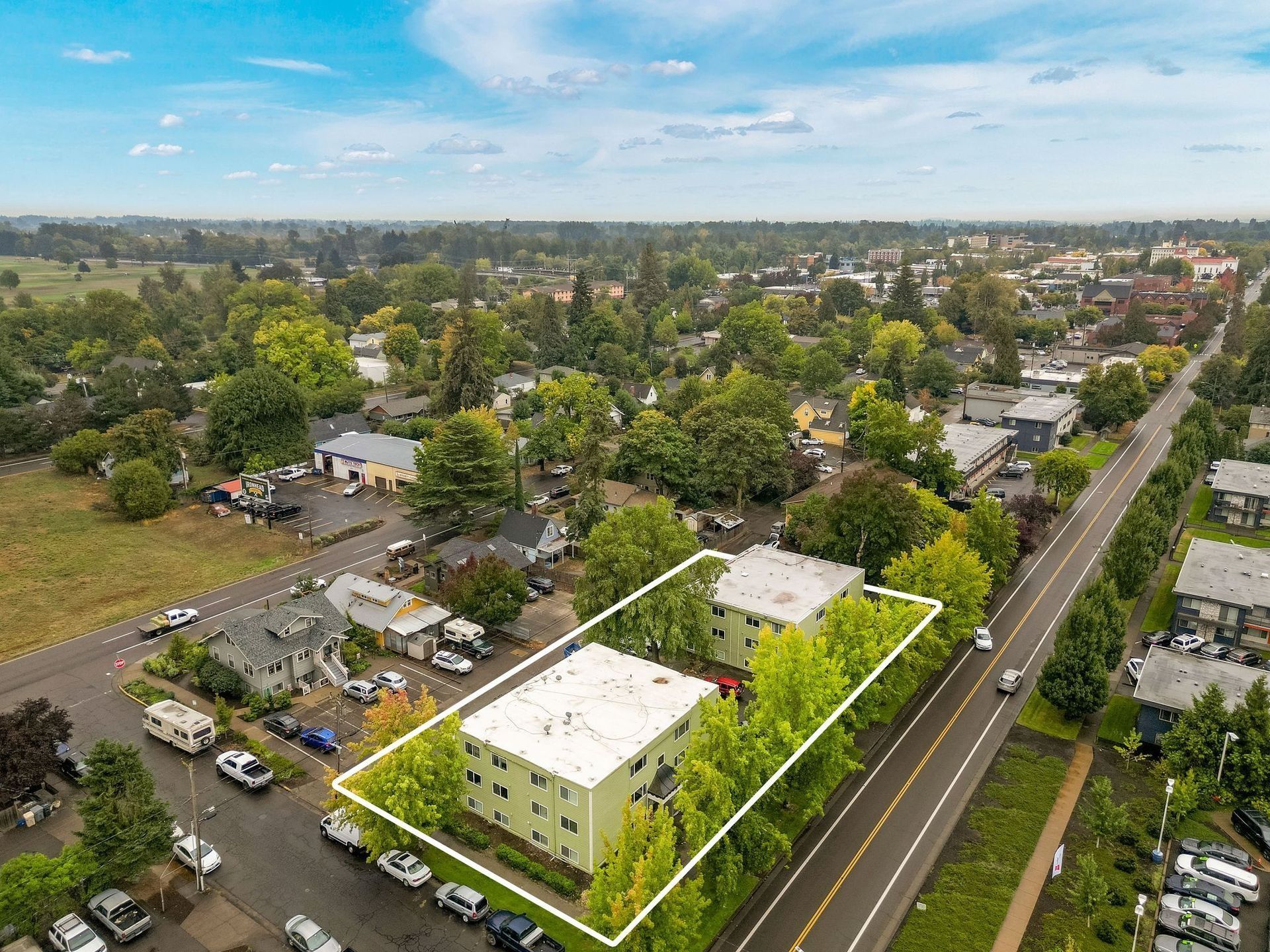 Aerial view of a neighborhood with a highlighted white building beside a road and trees