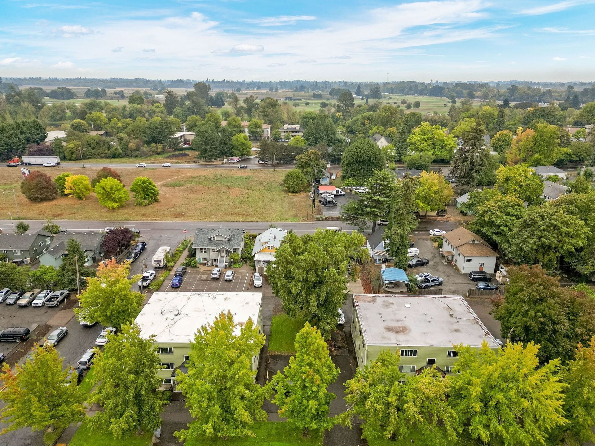 Aerial view of a suburban neighborhood with houses, trees, roads, and open fields under a blue sky