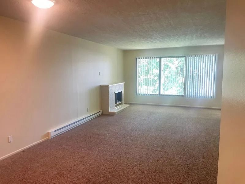 Empty beige living room with carpet, fireplace, and large window blinds
