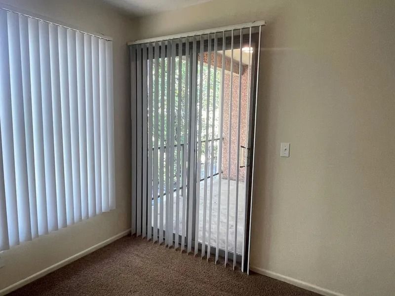 Empty room with vertical blinds and a sliding glass door opening to a patio