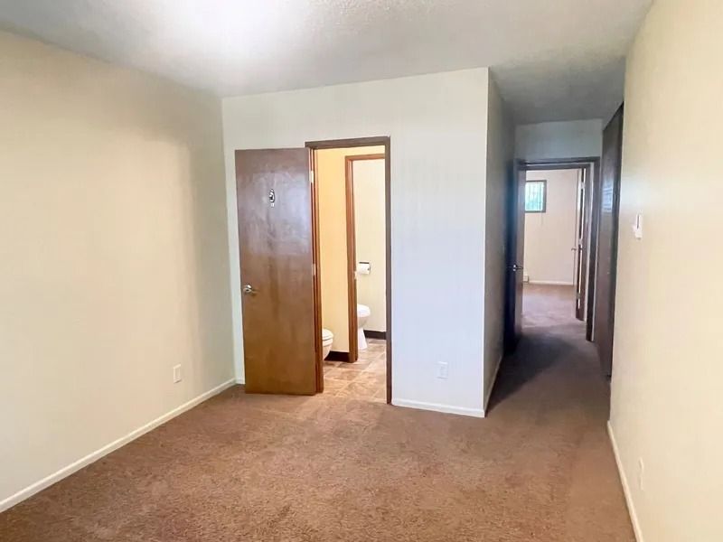 Empty beige bedroom with carpet, open closet door, and hallway view through a doorway