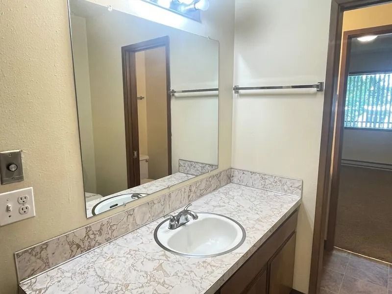 Bathroom vanity with sink, mirror, and beige granite countertop near a doorway