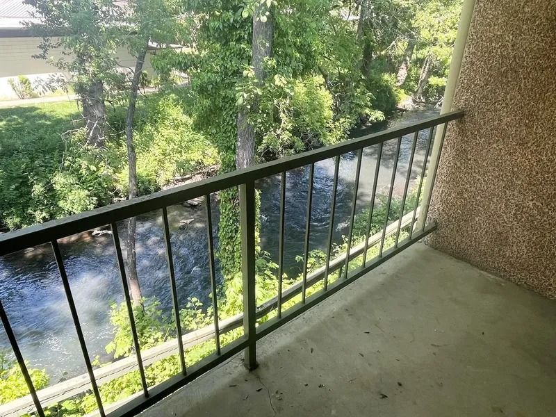 Balcony with black railing overlooking trees and a river below