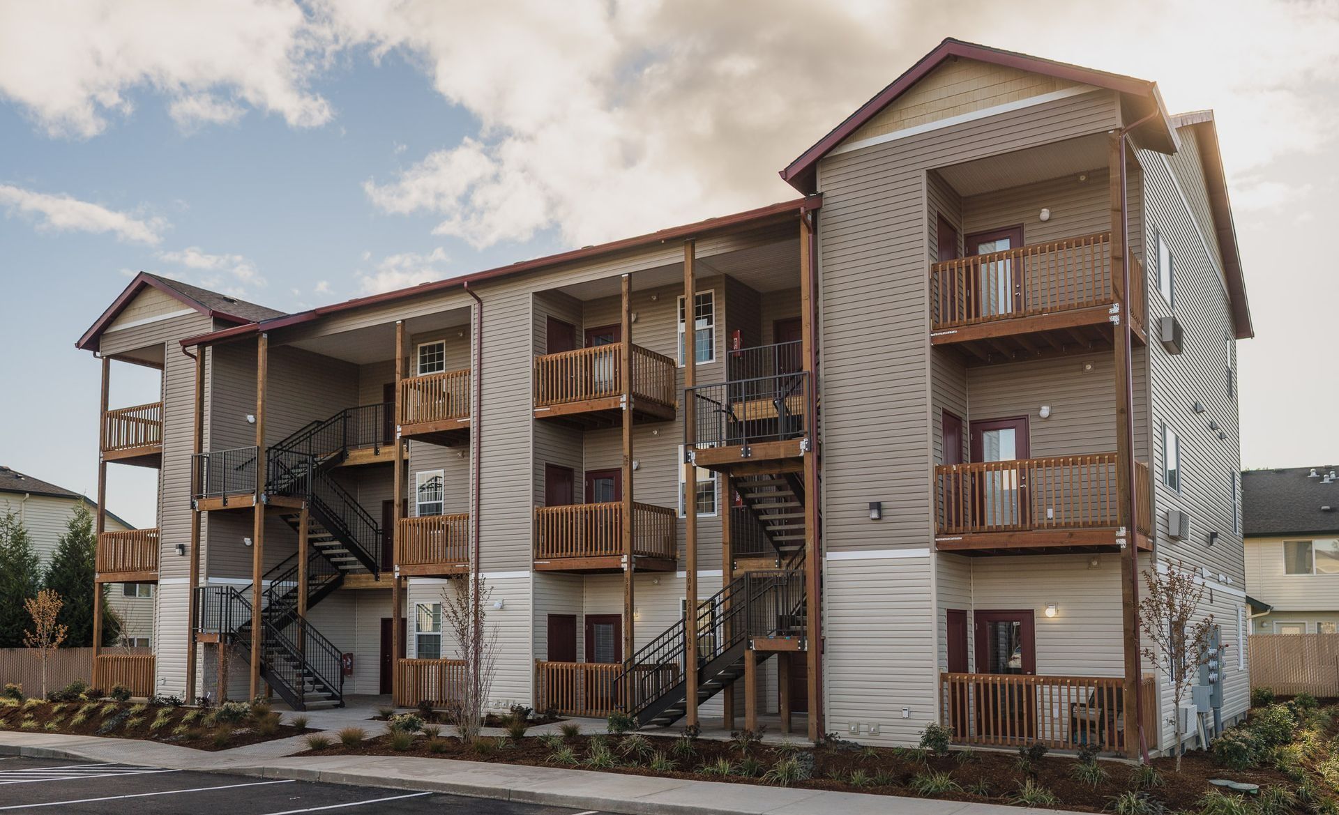 Three-story apartment building with balconies, wood siding, and a painted mural on the side under a cloudy sky