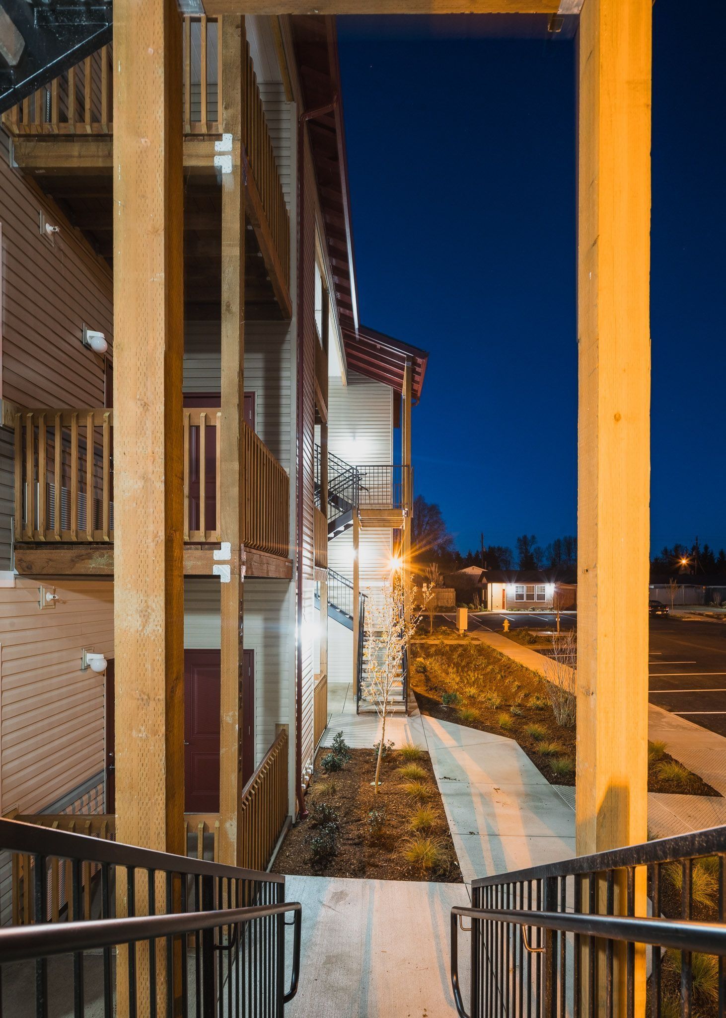 Apartment walkway at dusk with lit brick buildings, railings, and a snowy path under a deep blue sky