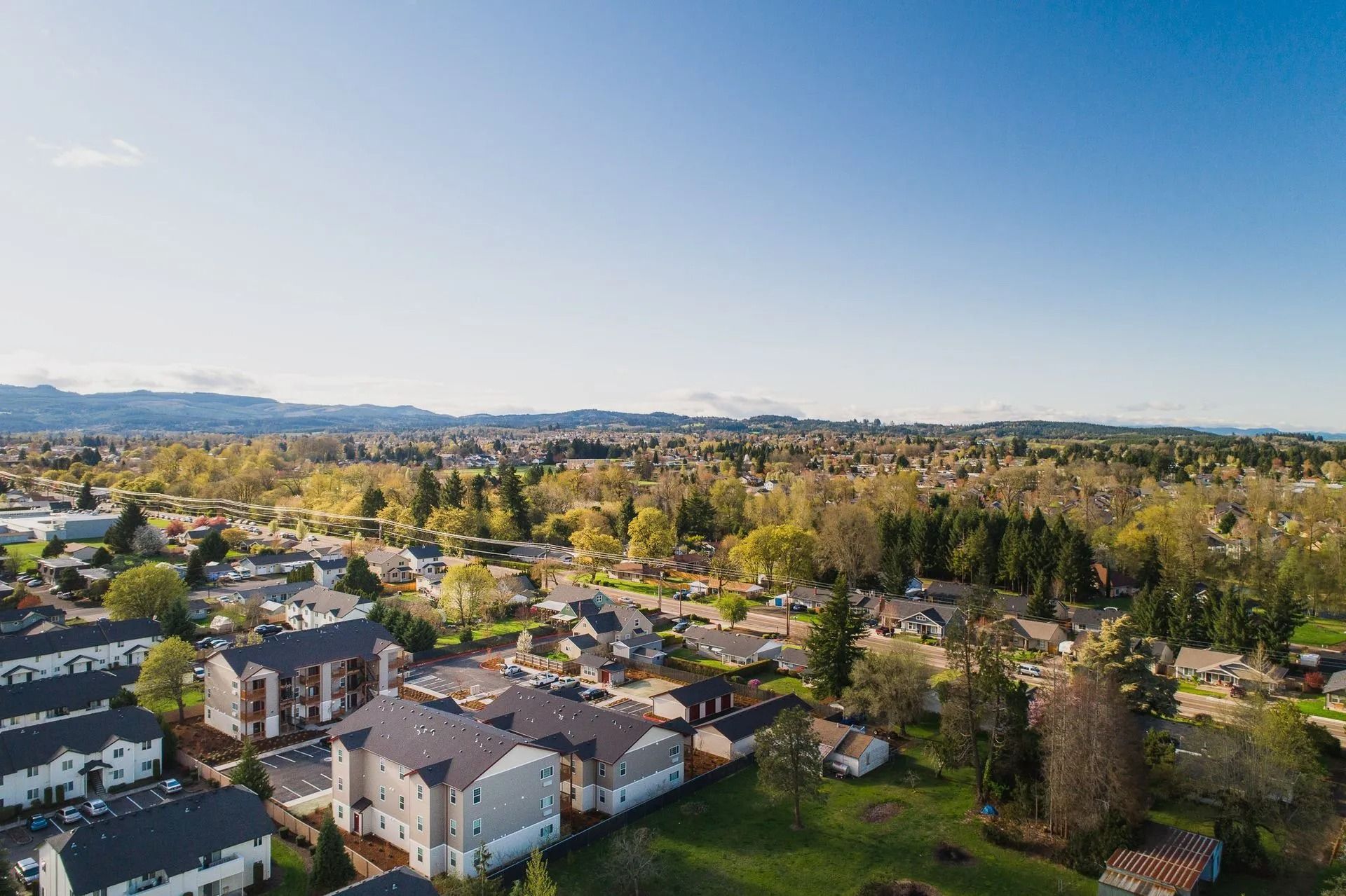 Aerial view of a suburban neighborhood with houses, trees, and distant hills under a clear blue sky