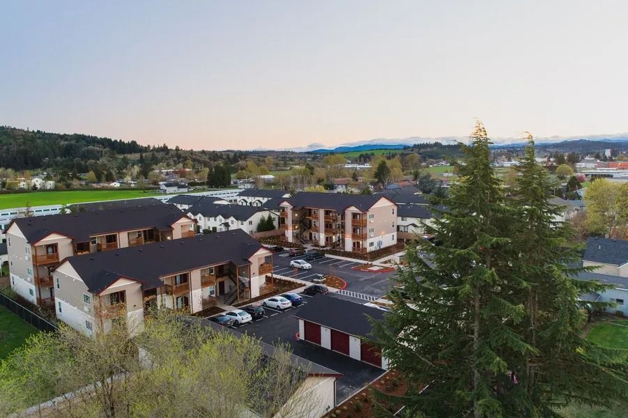 Aerial view of a residential complex with white buildings, parked cars, and trees at dusk