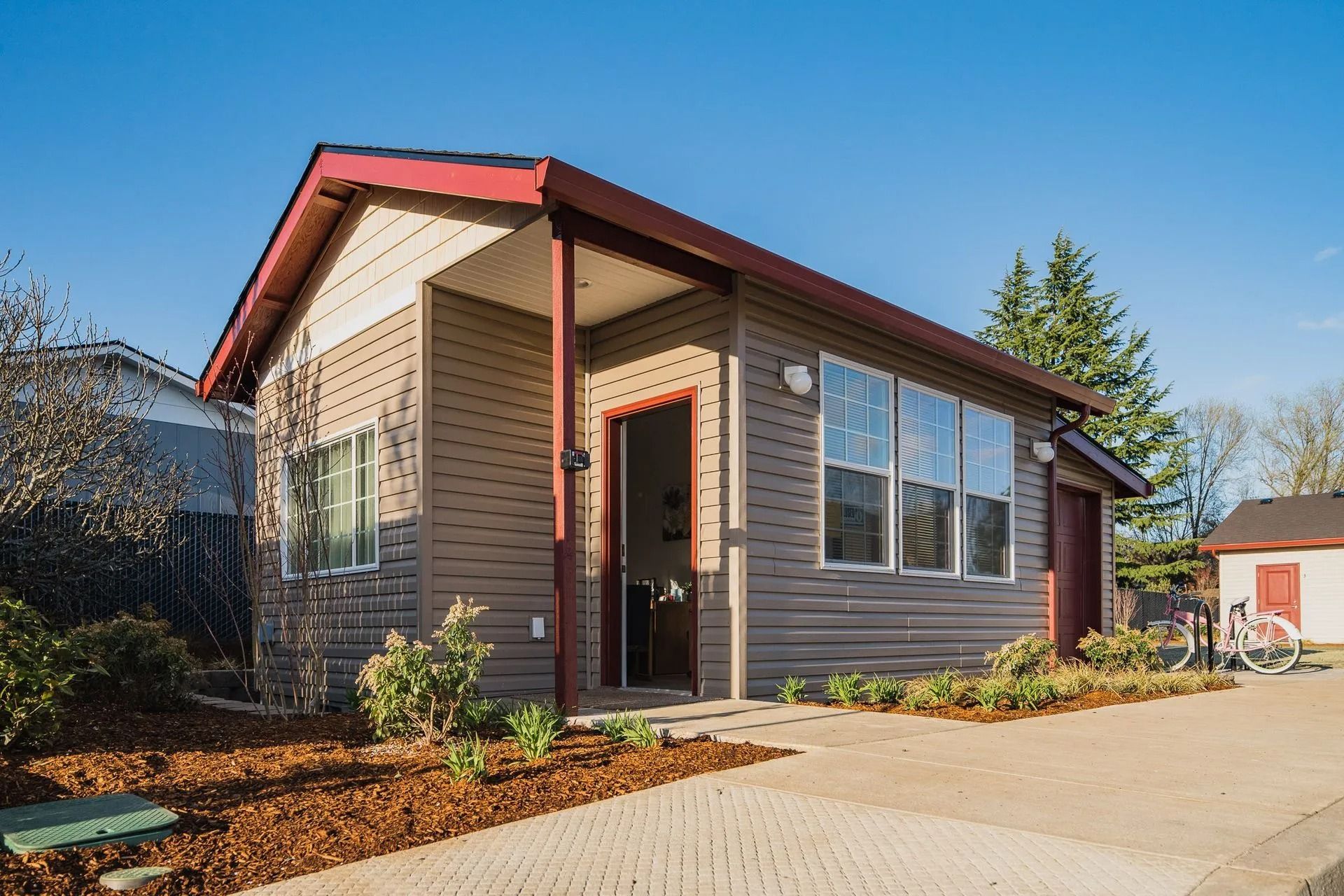 Small modern house with brown siding, red roof trim, and a paved driveway in daylight