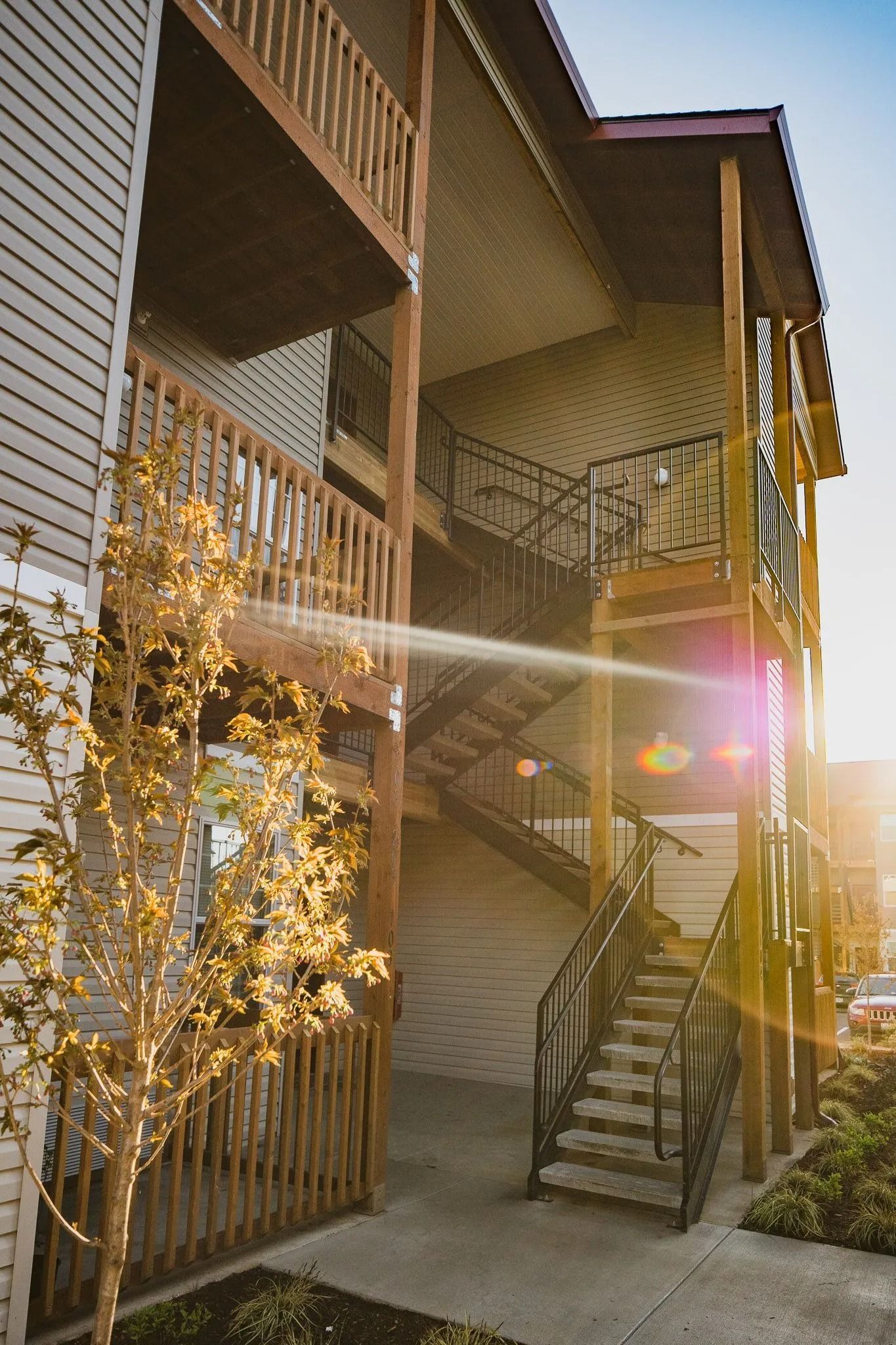 Apartment balconies and stairwell bathed in warm sunset light, with trees in the foreground