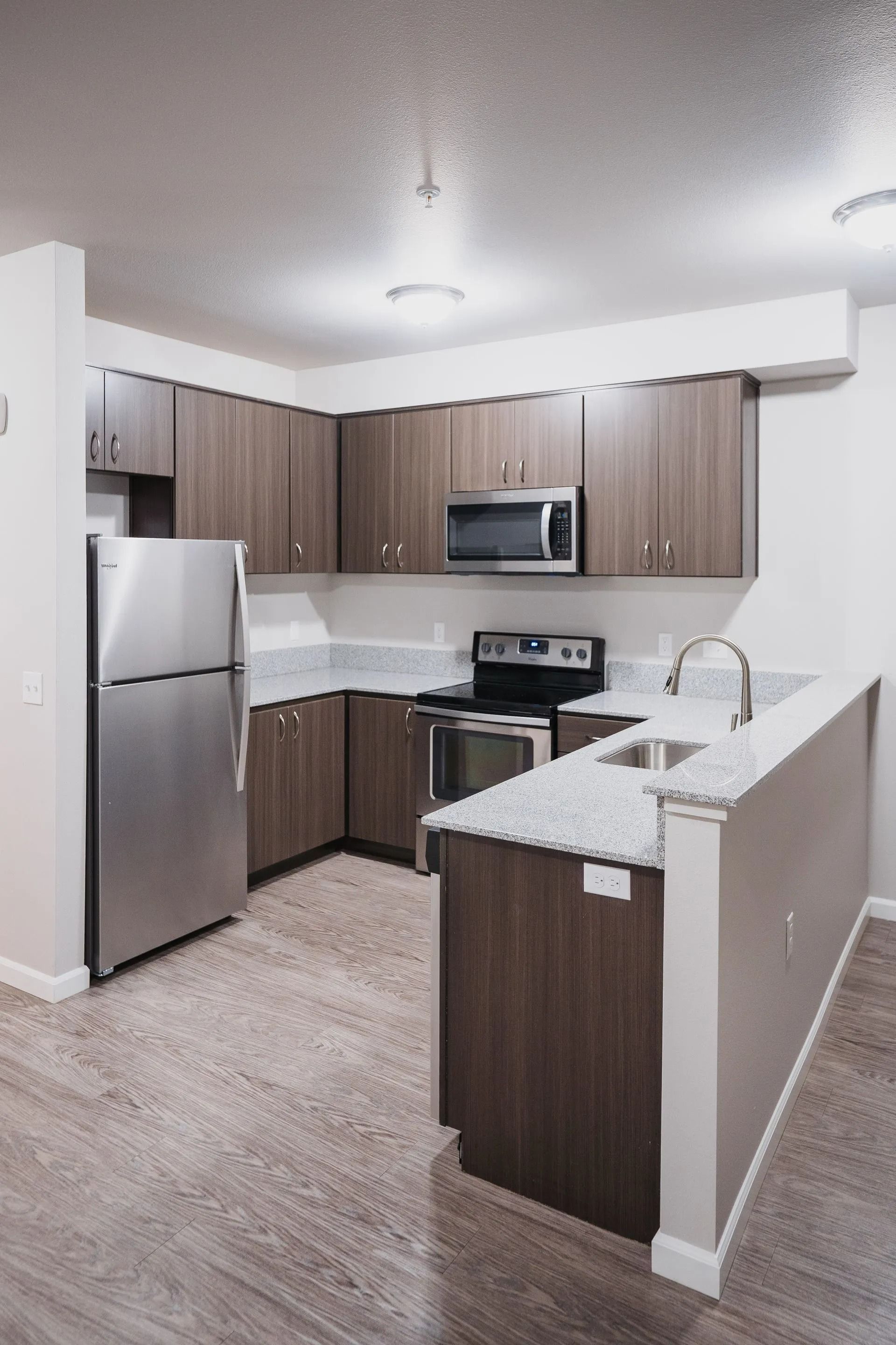 Modern kitchen with stainless appliances, dark wood cabinets, white countertops, and a breakfast bar