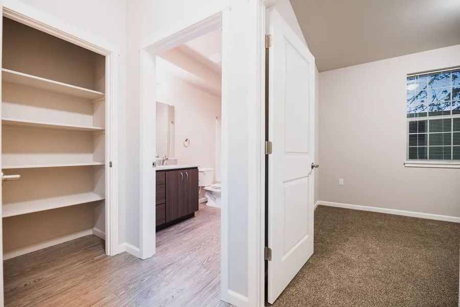 Empty bedroom with carpet, open closet shelves, and an attached bathroom visible through open doors