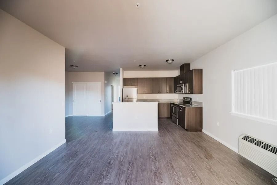 Empty modern apartment living room with kitchen, gray flooring, white walls, and large windows