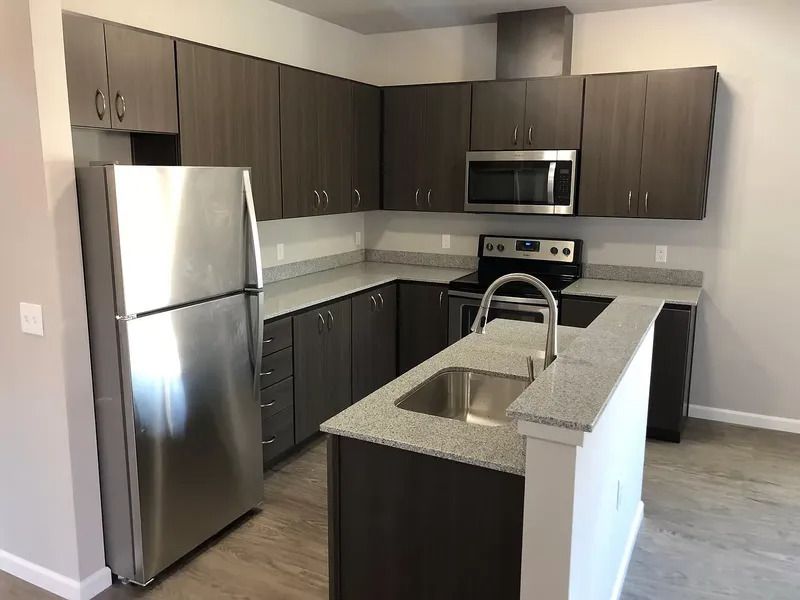 Modern kitchen with stainless steel appliances, dark cabinets, and a gray island with sink.