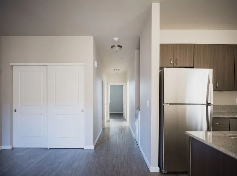 Bright apartment hallway beside a kitchen with stainless steel fridge and white closet doors.