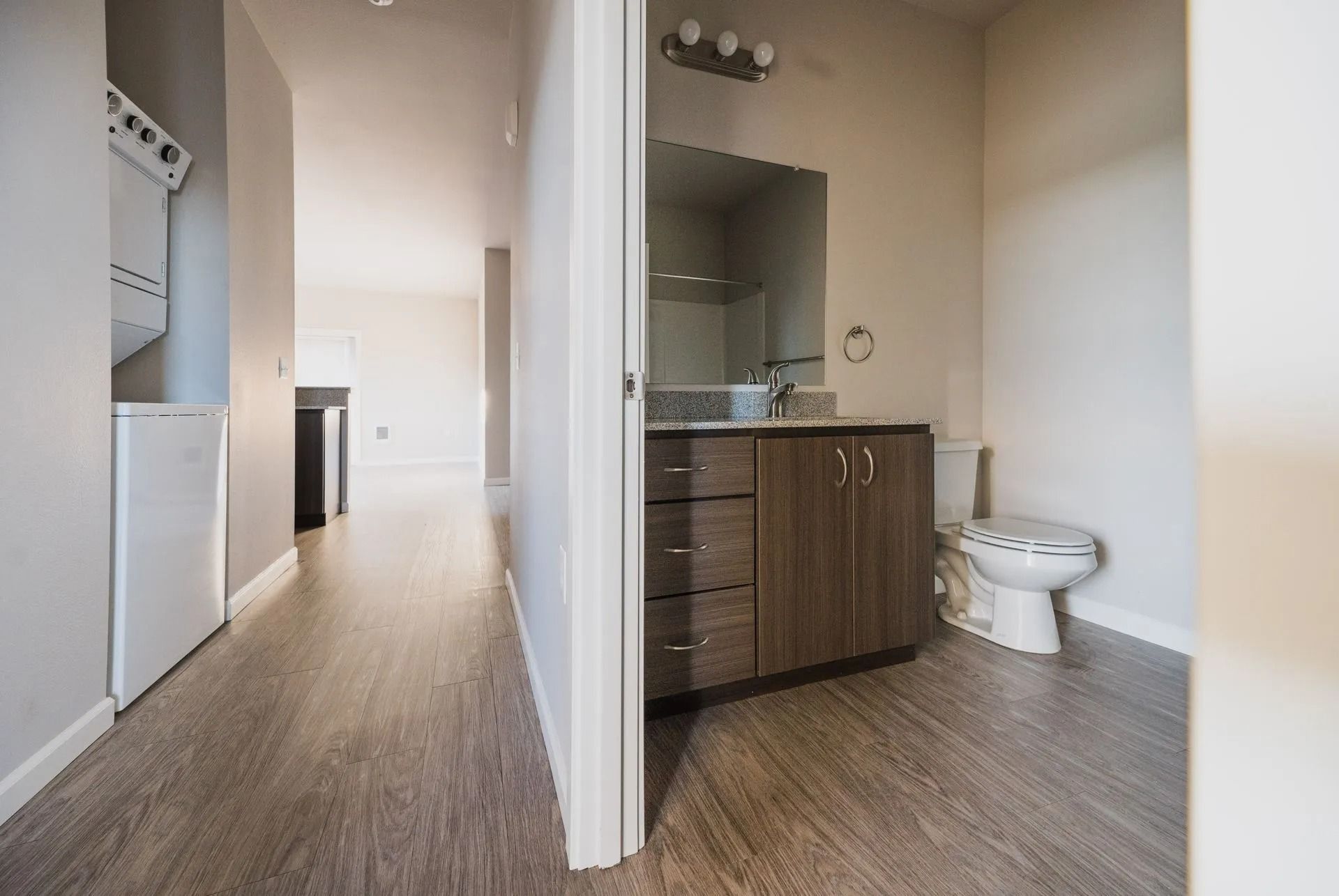Hallway view into a bathroom with wood cabinets, white toilet, and tiled floor