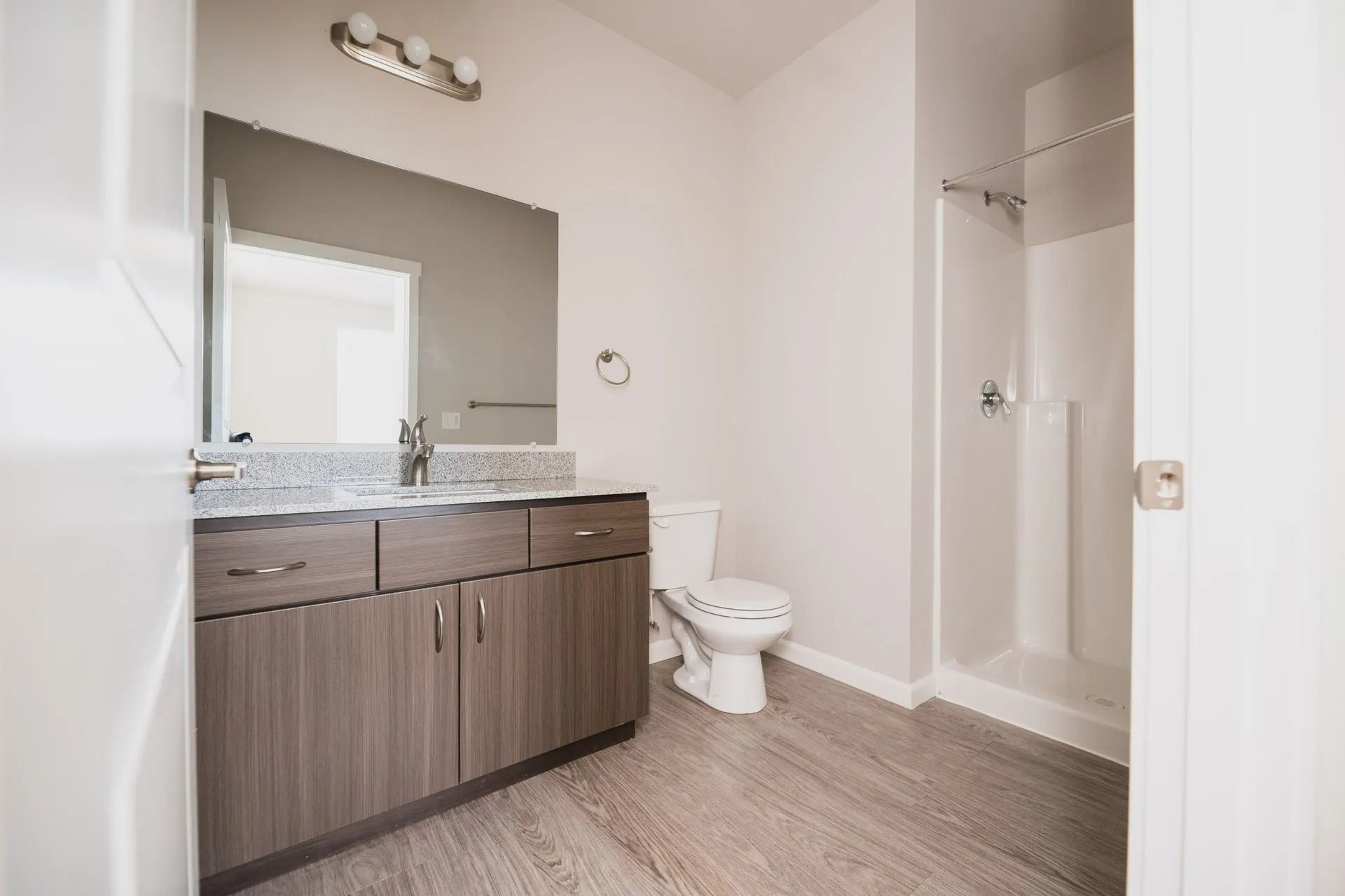 Modern bathroom with wood vanity, large mirror, toilet, and shower stall
