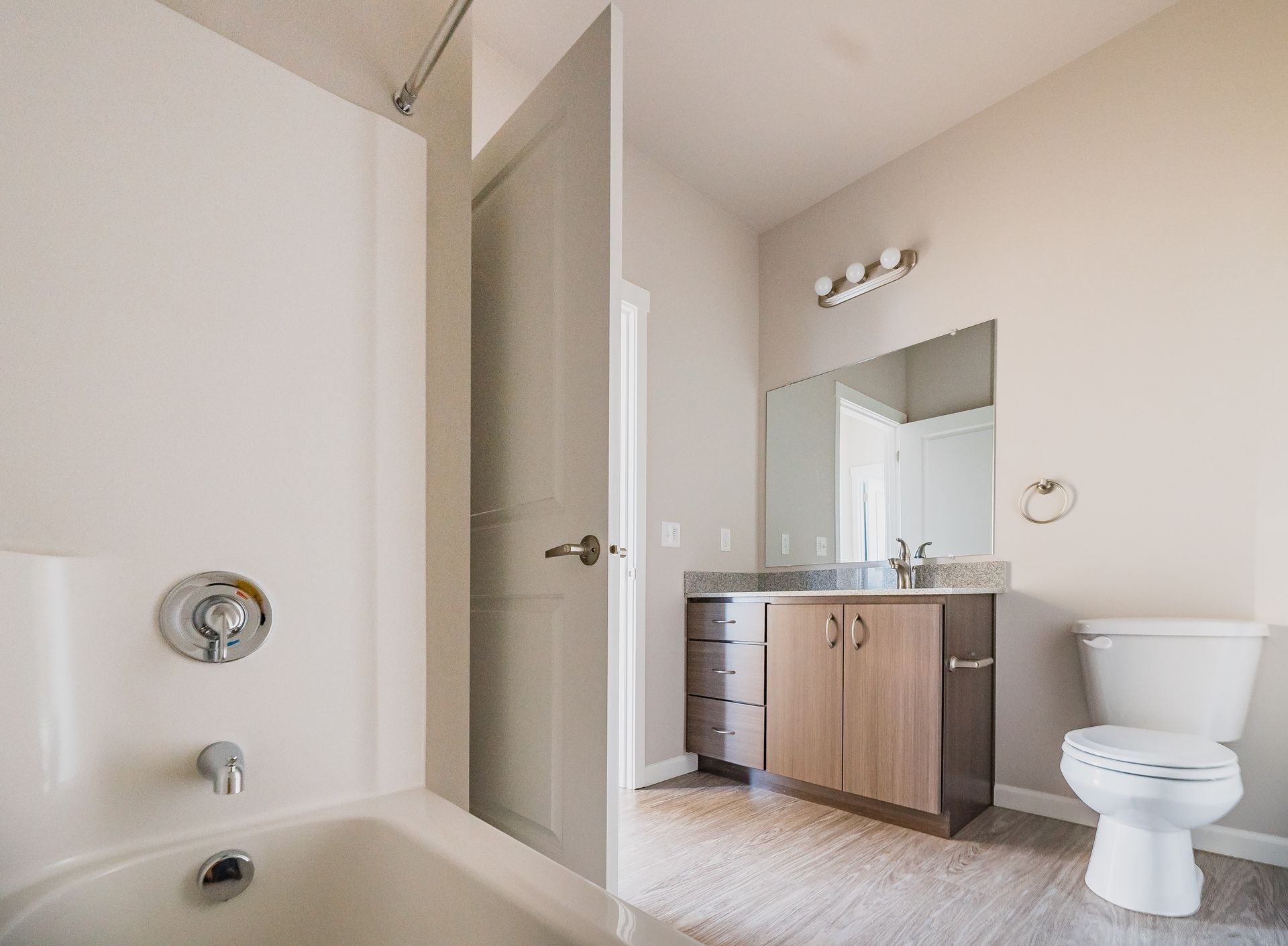 Bathroom with a tub, vanity sink, mirror, and toilet in a light beige room.