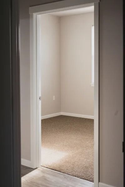 Open doorway to a carpeted empty room with beige walls and white trim