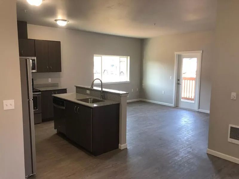 Empty modern kitchen and living area with dark cabinets, gray walls, and sliding glass door