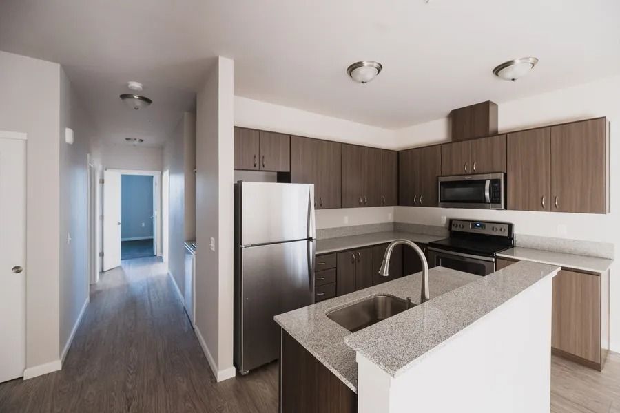 Modern kitchen with dark wood cabinets, stainless appliances, granite island, and hallway view