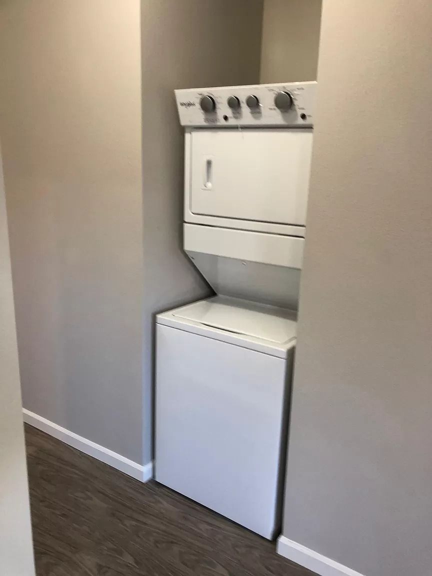 Stacked washer and dryer in a narrow hallway, with a white fridge below the washer.