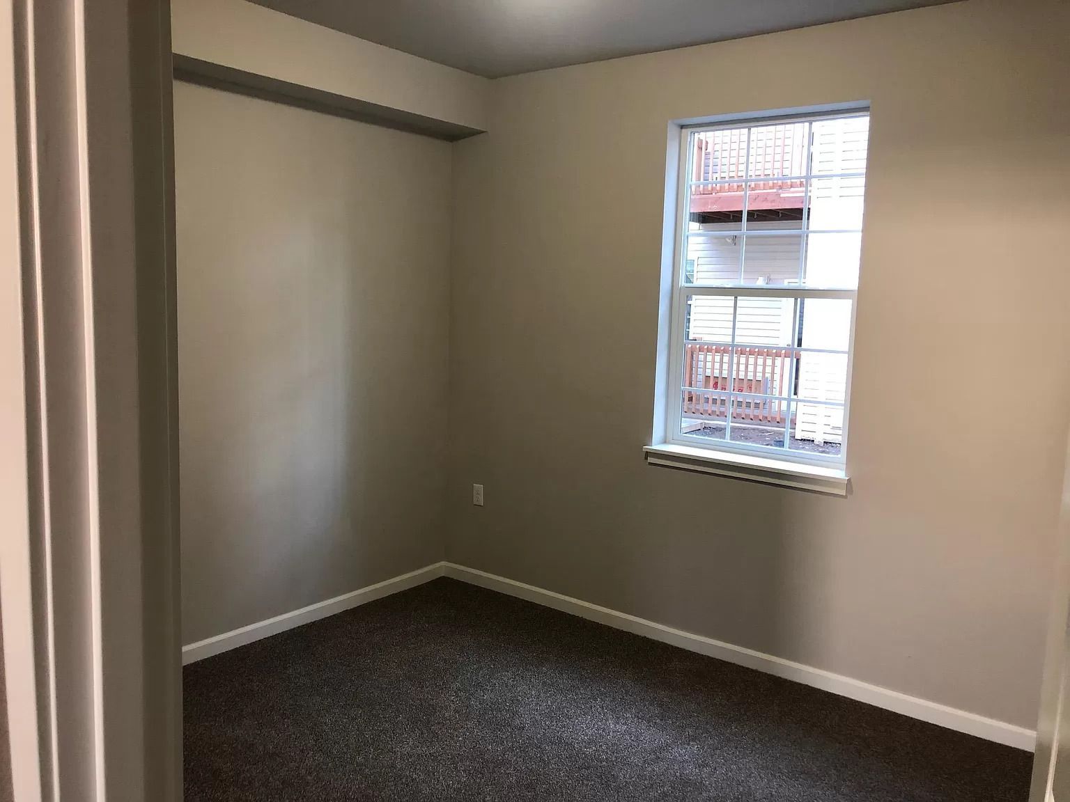 Empty beige room with dark carpet and a single window.
