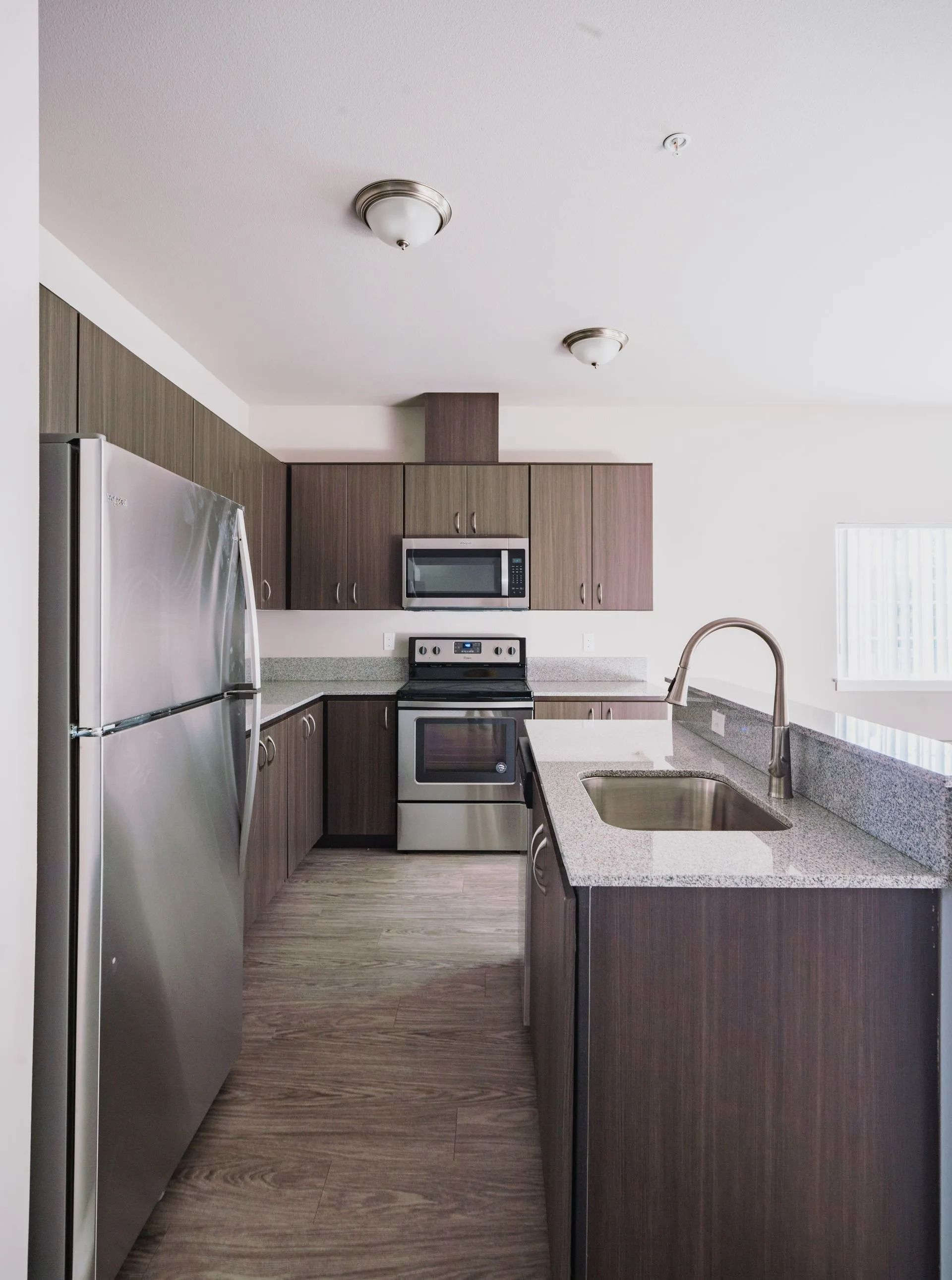 Modern kitchen with stainless steel appliances, dark wood cabinets, and a granite island and countertop.