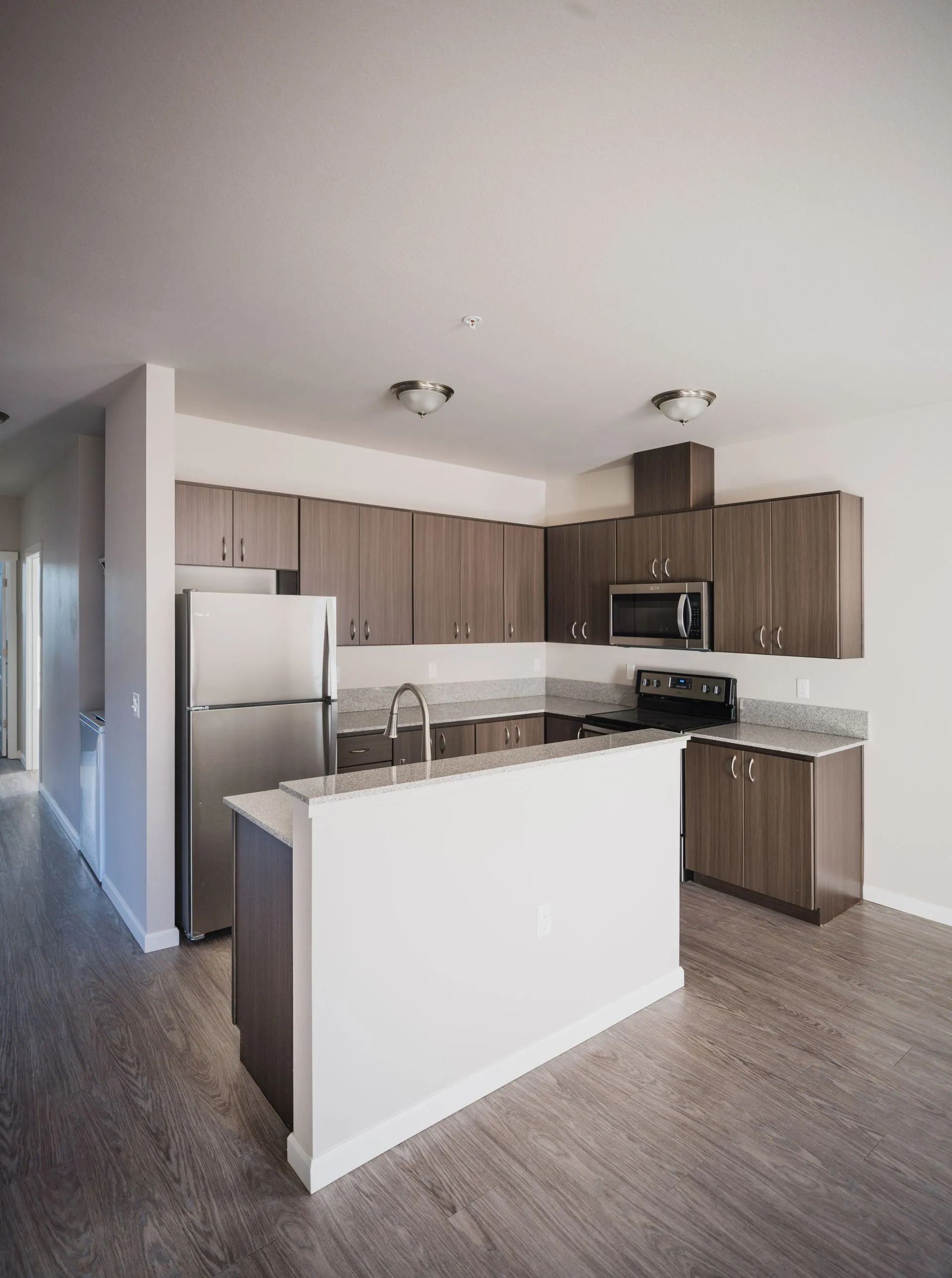 Modern kitchen with gray cabinets, stainless steel appliances, and a white island in an open apartment.