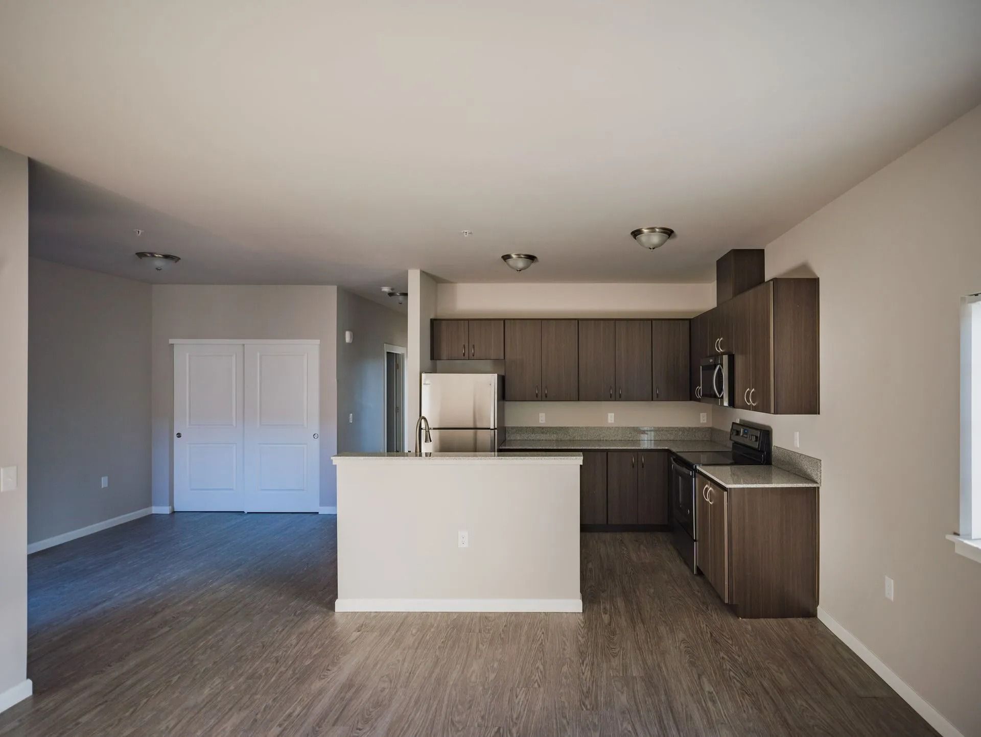 Empty open-plan kitchen and living area with wood cabinets, stainless appliances, and gray flooring
