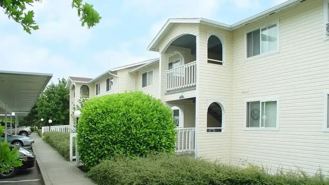Apartment courtyard with white buildings, balconies, and a walkway lined with greenery
