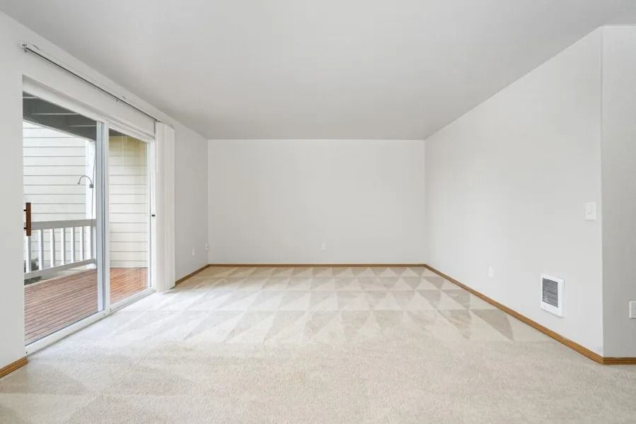 Empty white living room with carpet, sliding glass door, and window light