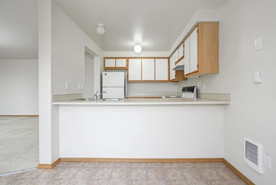Empty kitchen with white cabinets, light wood trim, and a breakfast bar in a bright apartment.