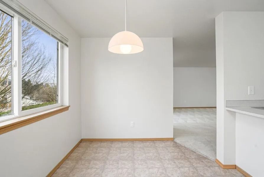 Empty bright room with white walls, tiled floor, large window, and hanging light fixture