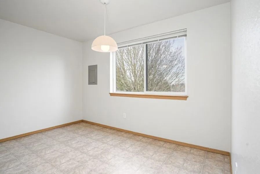 Empty white room with beige carpet, wood trim, window, and hanging ceiling light