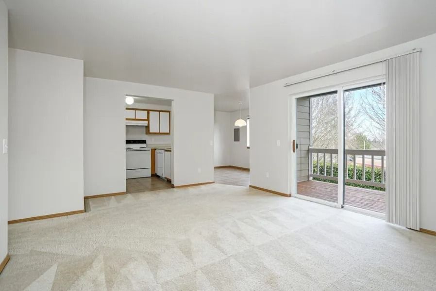 Bright empty living room with carpet, white walls, and sliding glass doors to a balcony
