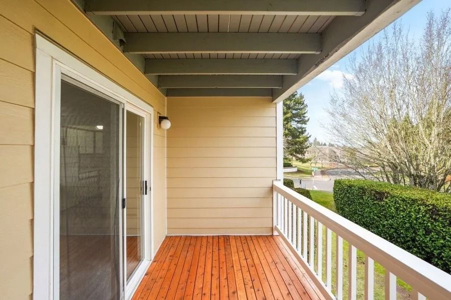 Covered wooden porch with sliding glass door, white railing, and yellow siding