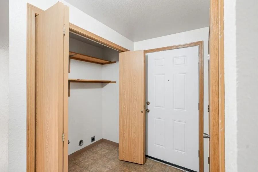 Empty closet with wood shelves and open doors beside a white entry door.