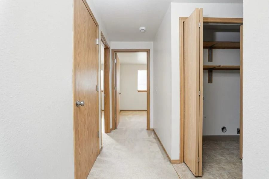 Hallway with open wooden doors and a small closet, showing a light carpeted interior.
