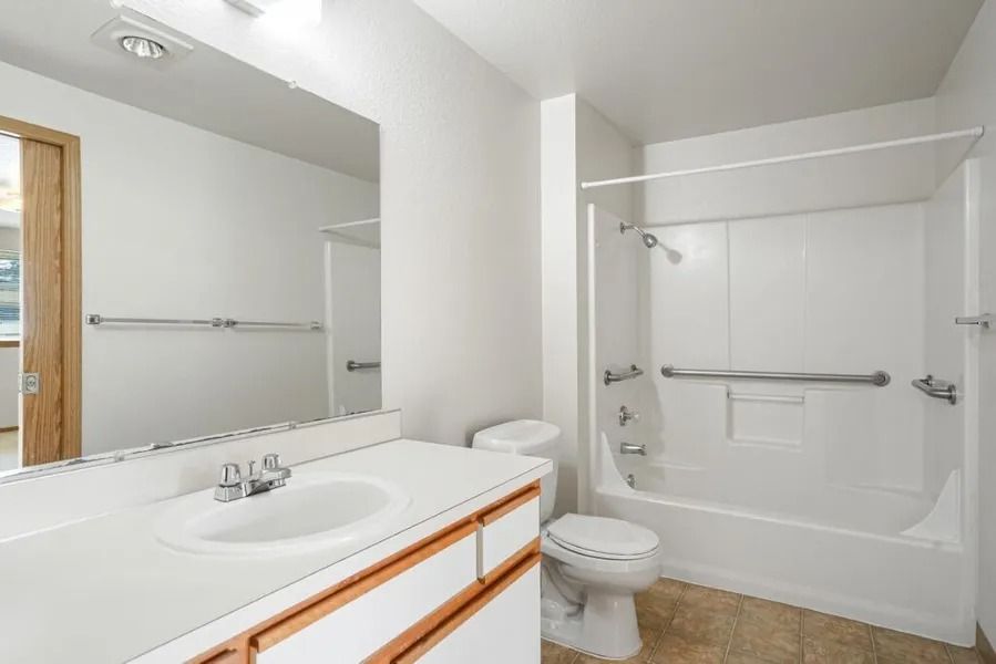 Bright bathroom with white vanity, toilet, and tub-shower combo on tan tile floor