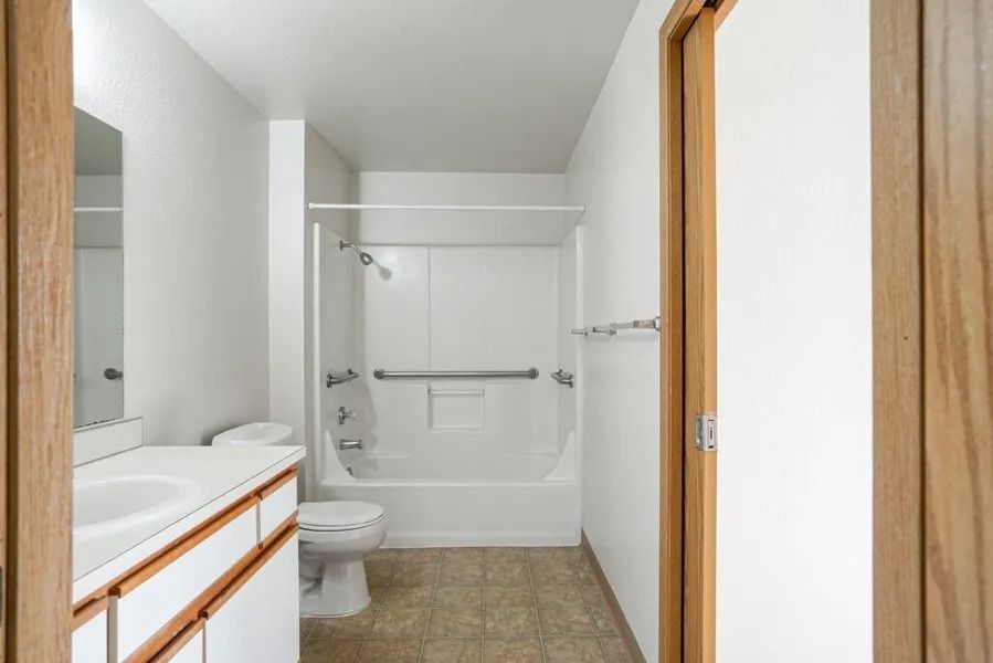 Small white bathroom with vanity, toilet, shower-tub combo, and towel bars on the wall.