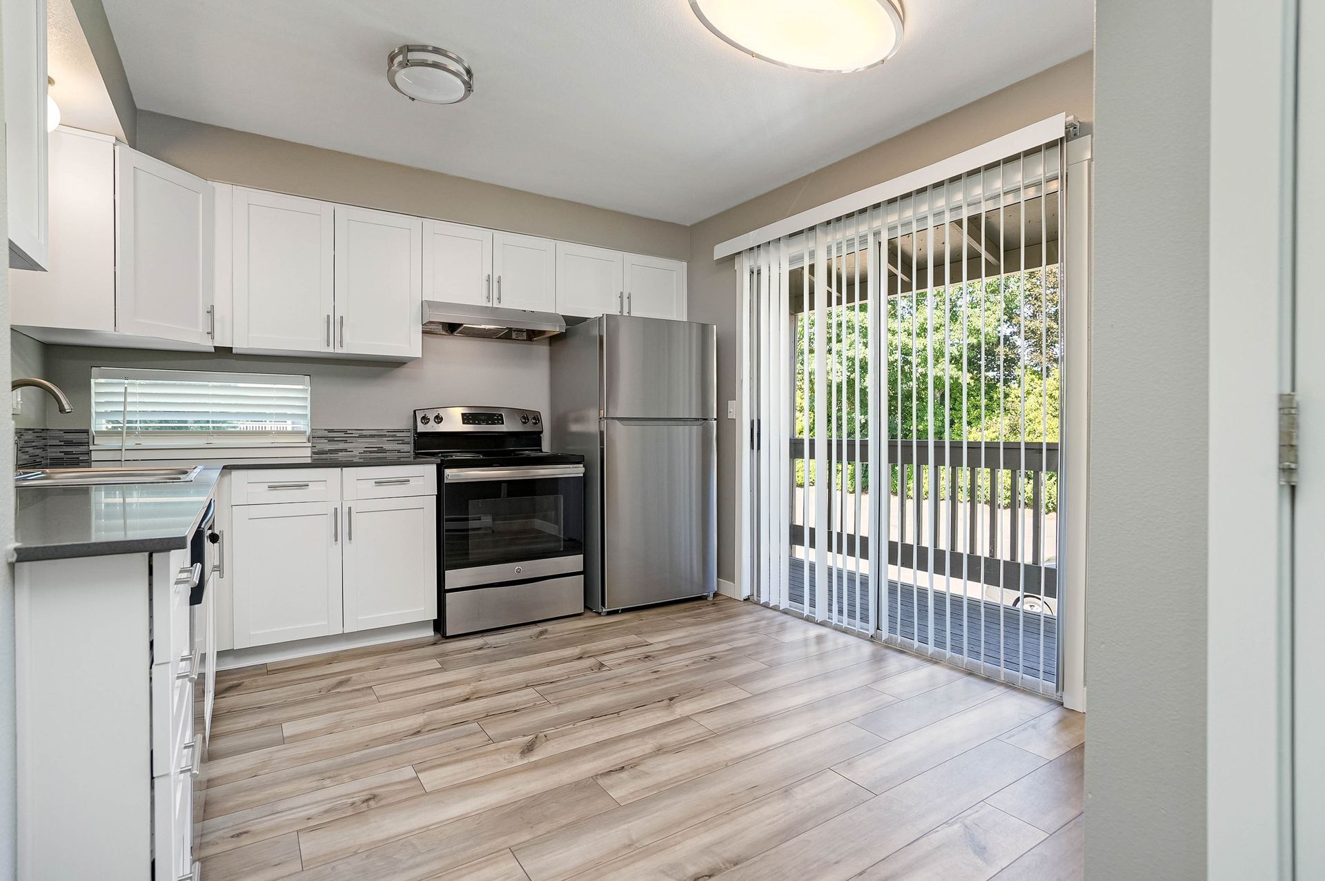Small modern kitchen with white cabinets, stainless appliances, and sliding glass doors with vertical blinds