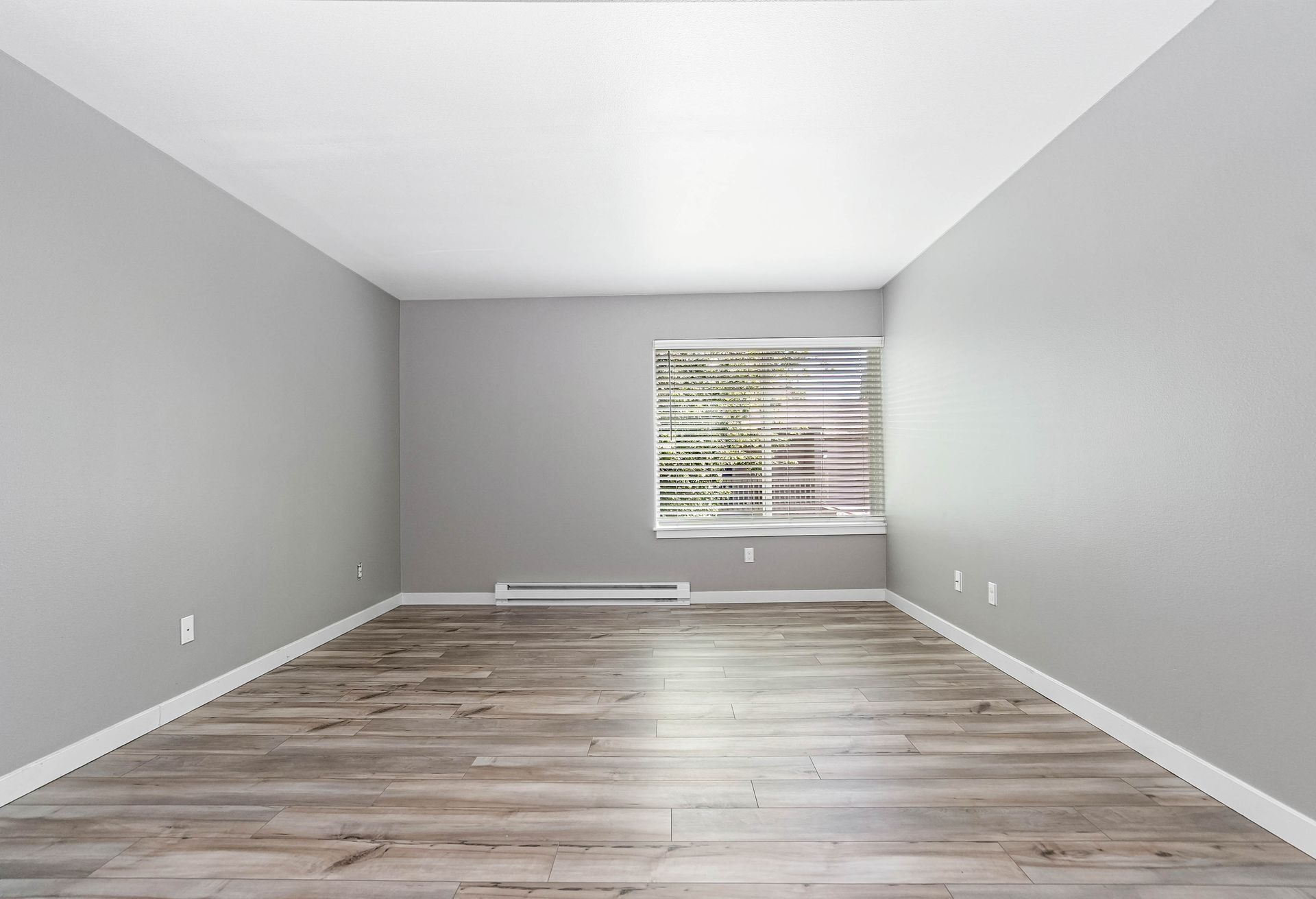 Empty gray room with wood-look floors and a window on the far wall