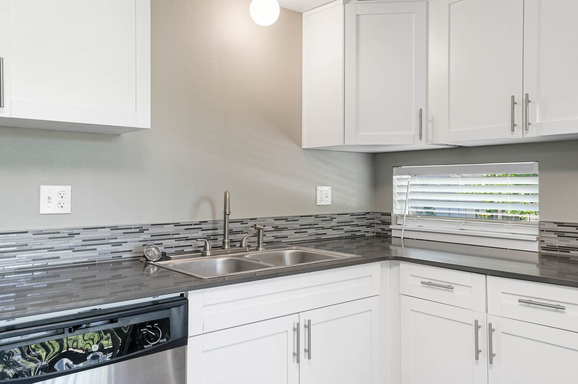 Modern white kitchen with stainless sink, gray mosaic backsplash, and white cabinets