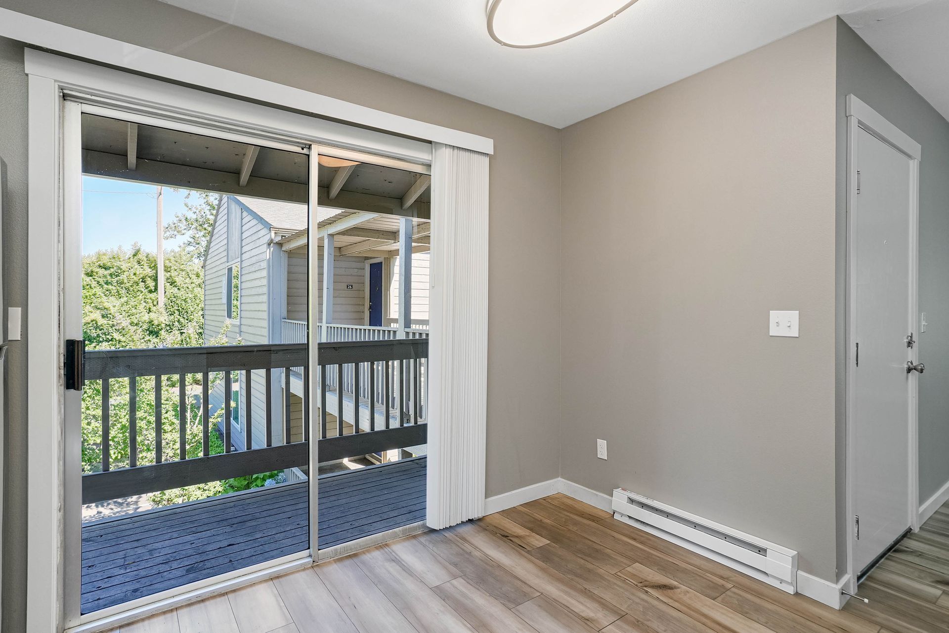 Empty apartment room with sliding glass door, balcony view, gray walls, and wood flooring