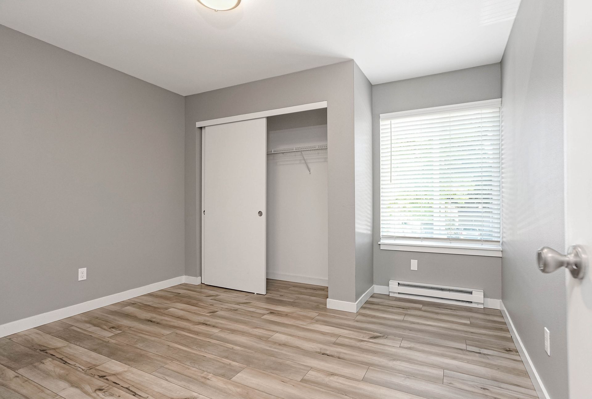 Empty gray bedroom with open closet and window blinds, wood-look floor, and white trim