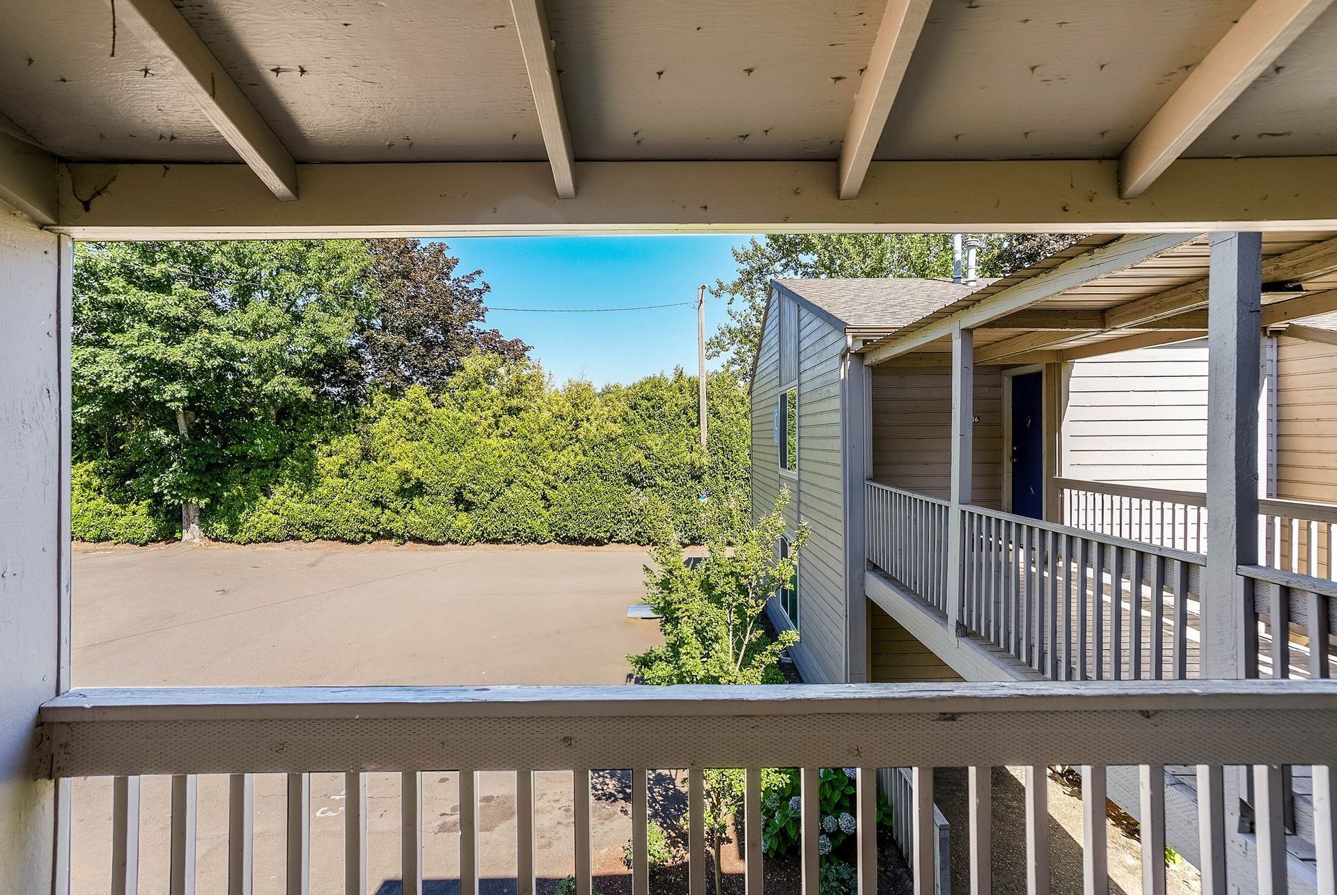 View from a covered porch overlooking a quiet courtyard, greenery, and adjacent apartment balconies.