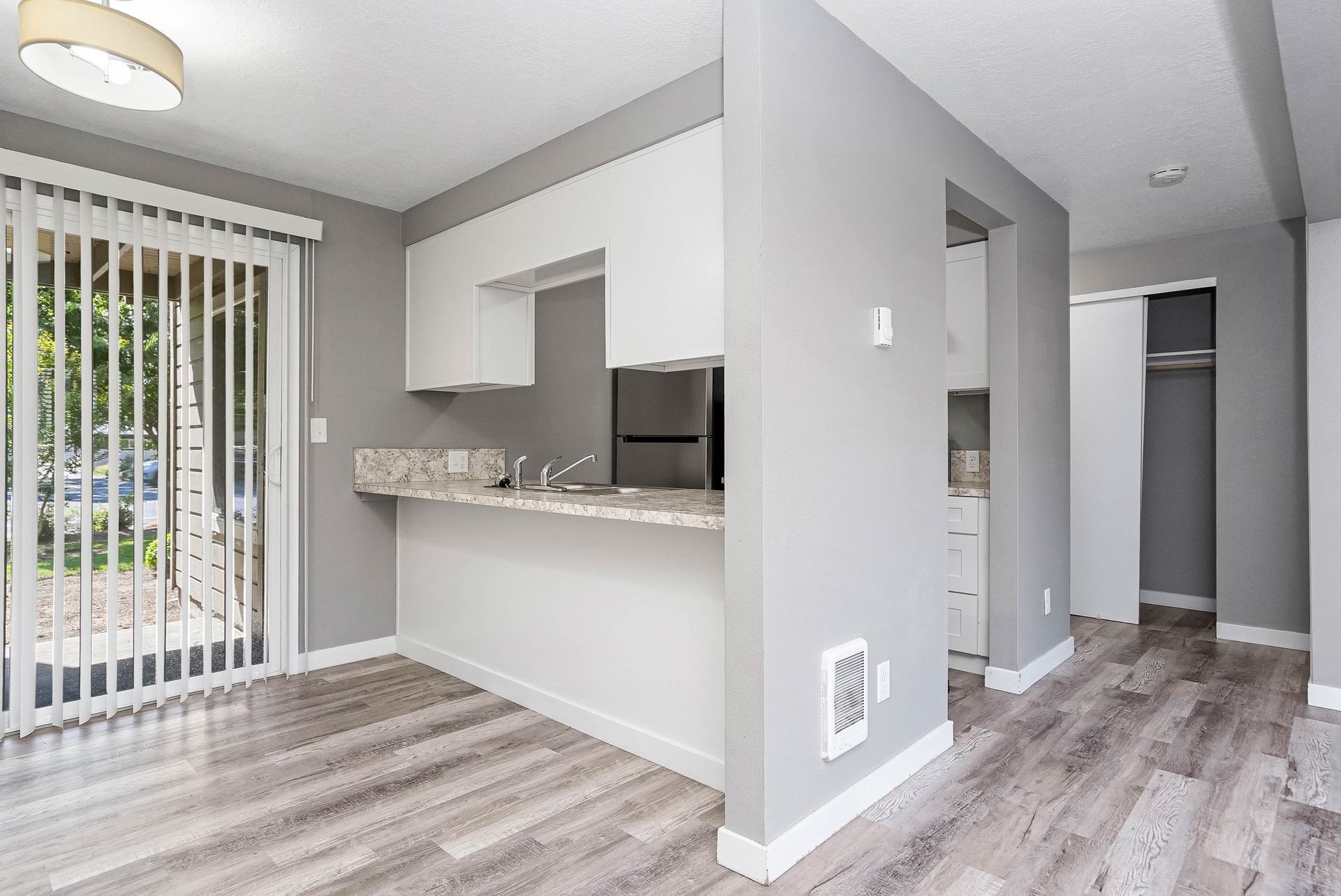 Empty modern apartment kitchen and dining area with gray flooring, white walls, and sliding glass door.